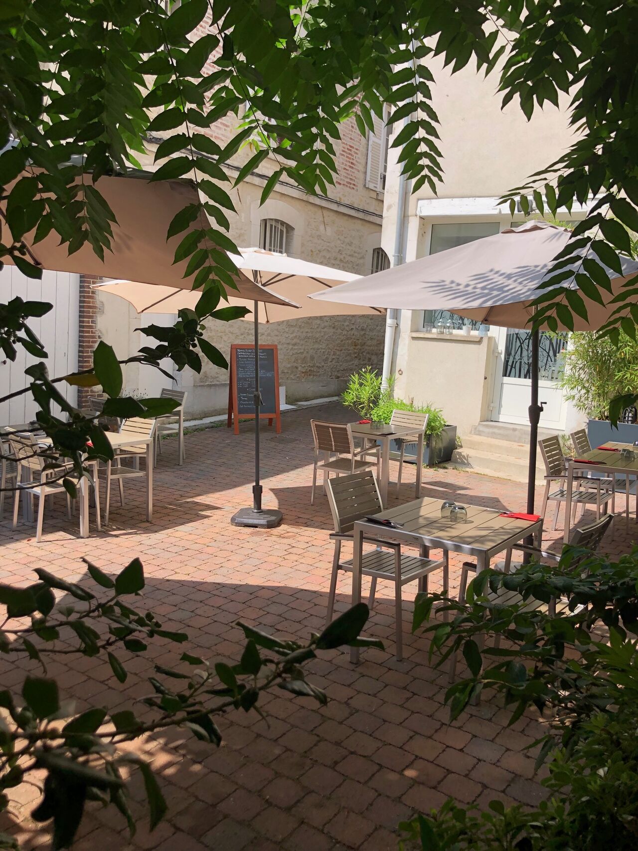 La grande terrasse extérieure ombragée, cour pavée et arbre